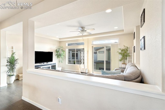 living area with a tray ceiling, dark wood finished floors, recessed lighting, a ceiling fan, and baseboards