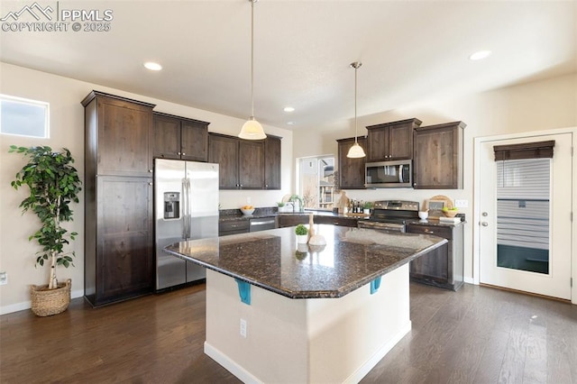 kitchen featuring dark wood finished floors, appliances with stainless steel finishes, dark stone countertops, a center island, and pendant lighting