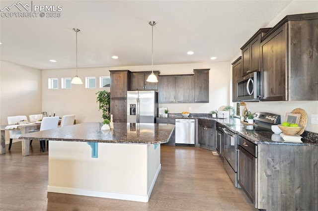 kitchen featuring dark wood-style floors, a center island, decorative light fixtures, stainless steel appliances, and dark brown cabinets