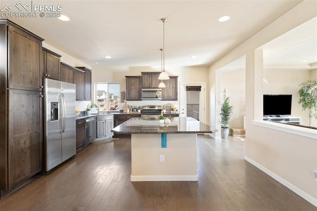 kitchen with dark brown cabinetry, dark stone counters, a center island, hanging light fixtures, and stainless steel appliances