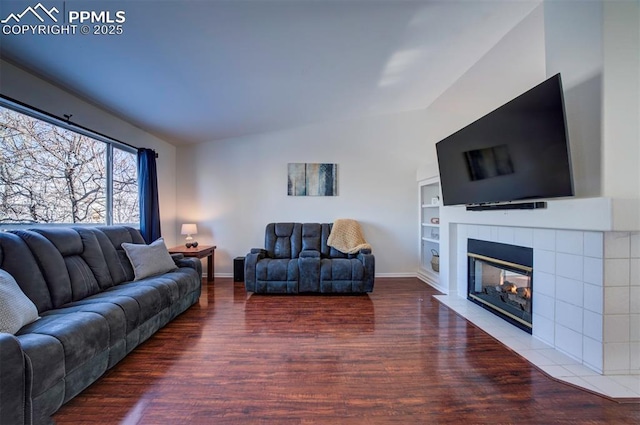 living room with built in features, a tile fireplace, vaulted ceiling, and hardwood / wood-style floors