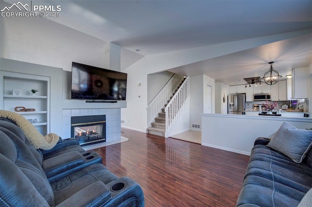 living room featuring lofted ceiling, dark wood-type flooring, built in features, a fireplace, and a chandelier