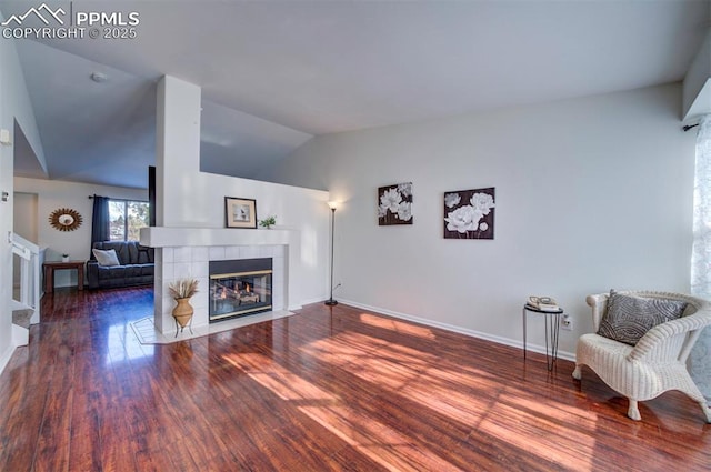 living room with a tiled fireplace, dark wood-type flooring, and vaulted ceiling