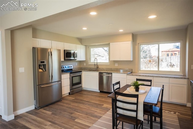 kitchen with appliances with stainless steel finishes, dark hardwood / wood-style floors, white cabinetry, sink, and light stone counters