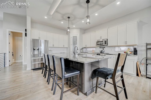 kitchen with stainless steel appliances, white cabinets, and a center island with sink