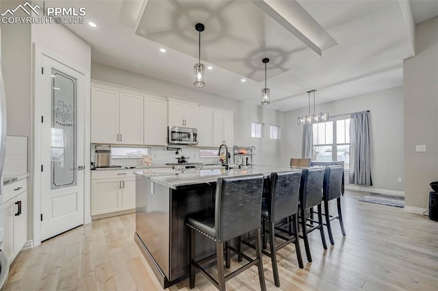 kitchen with a breakfast bar, white cabinetry, hanging light fixtures, light stone counters, and an island with sink