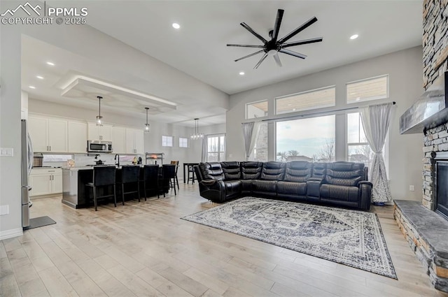 living room featuring a stone fireplace, ceiling fan with notable chandelier, and light hardwood / wood-style floors