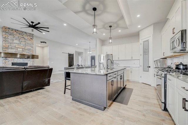 kitchen featuring appliances with stainless steel finishes, a center island with sink, white cabinets, and decorative light fixtures