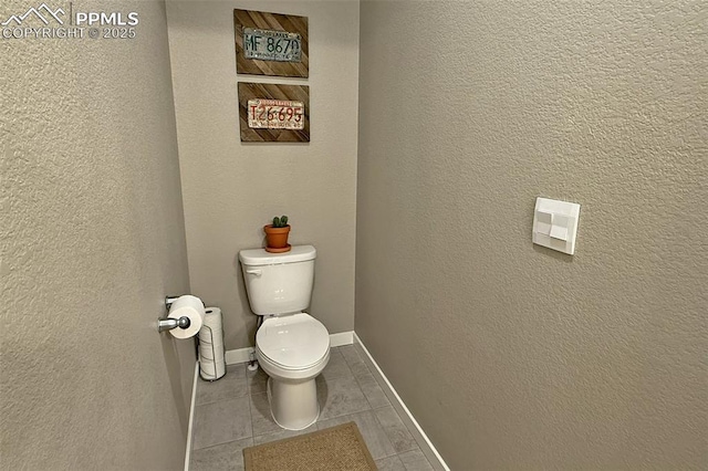 bathroom with tile patterned flooring, baseboards, a textured wall, and toilet