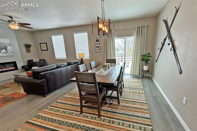 dining area featuring ceiling fan with notable chandelier, a large fireplace, baseboards, and wood finished floors