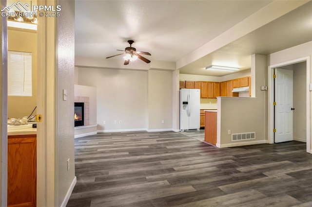 unfurnished living room with ceiling fan, dark hardwood / wood-style floors, and a tiled fireplace