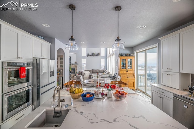 kitchen with appliances with stainless steel finishes, white cabinetry, sink, hanging light fixtures, and light stone counters