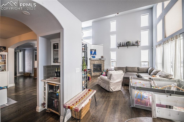 living room with a high ceiling, dark wood-type flooring, beverage cooler, and a fireplace