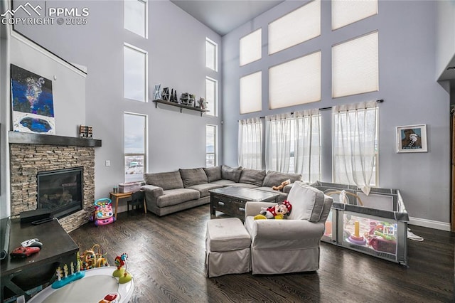 living room featuring dark hardwood / wood-style floors, a towering ceiling, and a stone fireplace