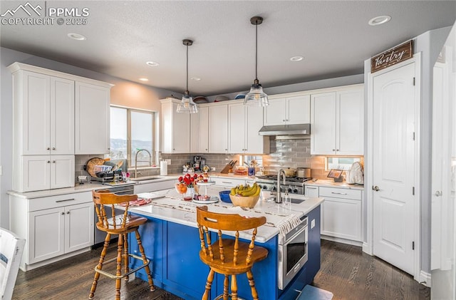 kitchen featuring pendant lighting, sink, white cabinetry, stainless steel appliances, and an island with sink