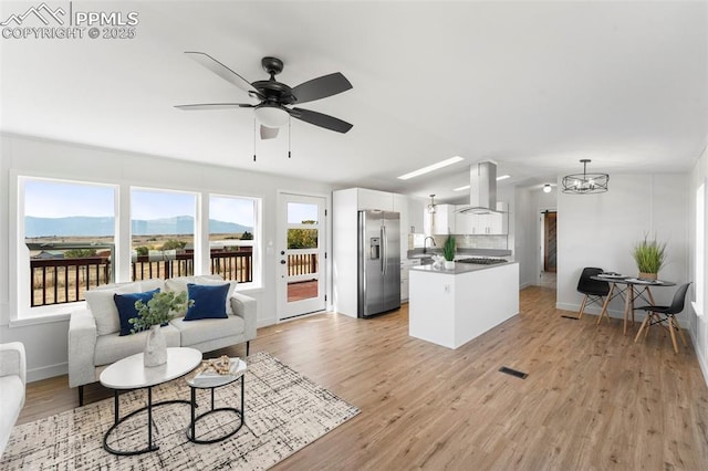 living room with ceiling fan with notable chandelier, a mountain view, vaulted ceiling, and light wood-type flooring