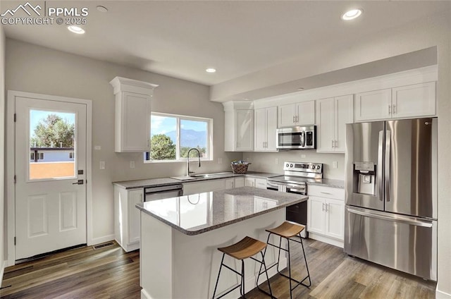 kitchen with stainless steel appliances, dark wood-style flooring, a sink, and a kitchen island