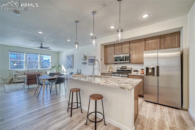 kitchen featuring an island with sink, appliances with stainless steel finishes, sink, and hanging light fixtures