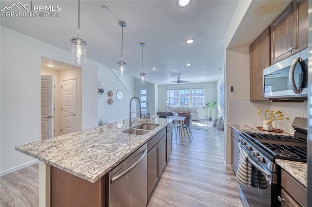 kitchen with sink, decorative light fixtures, an island with sink, stainless steel appliances, and backsplash