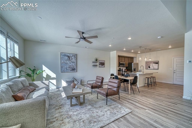 living room featuring ceiling fan, a textured ceiling, and light wood-type flooring