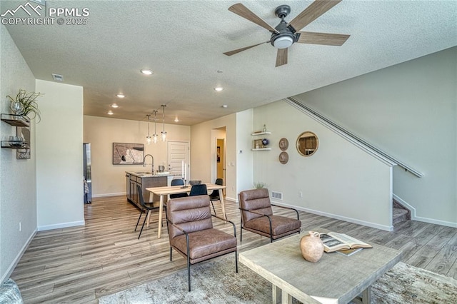 living room with ceiling fan, sink, a textured ceiling, and light wood-type flooring