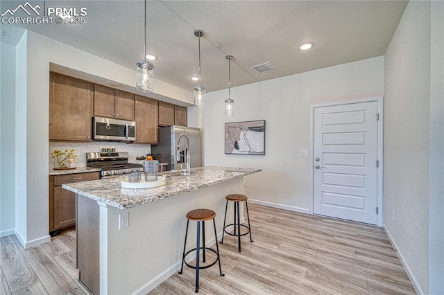 kitchen with a breakfast bar area, light stone counters, a center island with sink, stainless steel appliances, and light hardwood / wood-style floors