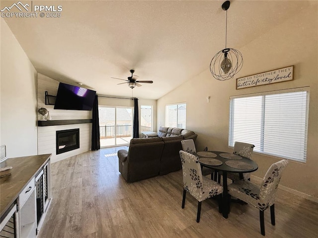 dining area with lofted ceiling, ceiling fan, wood-type flooring, a large fireplace, and a textured ceiling