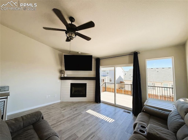 living room featuring light hardwood / wood-style flooring, a large fireplace, and ceiling fan