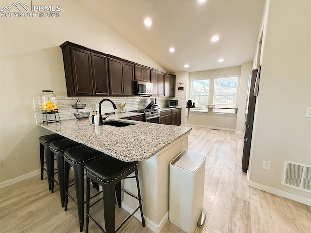 kitchen featuring sink, appliances with stainless steel finishes, dark brown cabinets, light stone countertops, and a kitchen bar