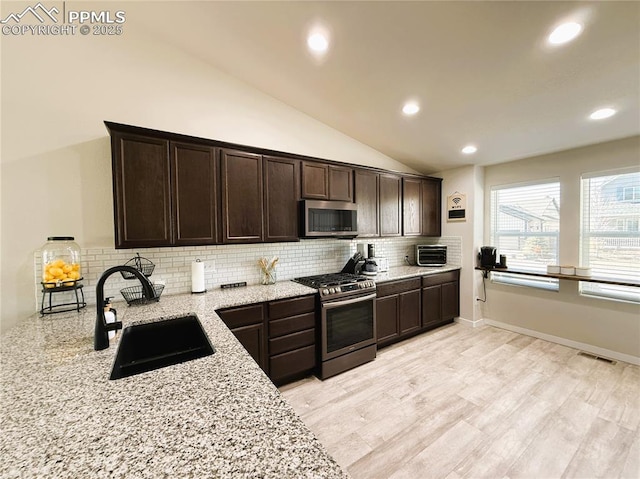 kitchen with light stone counters, sink, stainless steel appliances, and dark brown cabinetry