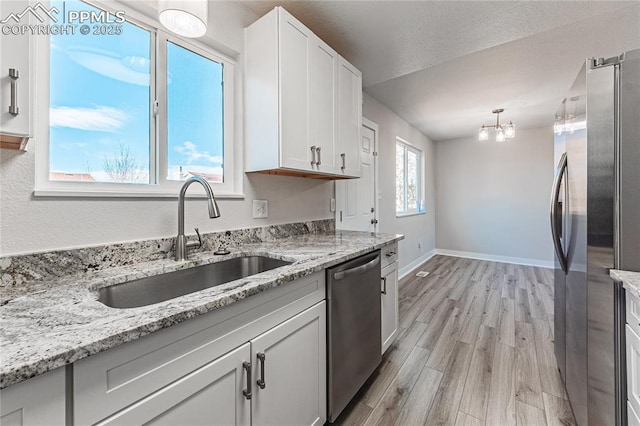 kitchen featuring white cabinetry, appliances with stainless steel finishes, decorative light fixtures, and sink