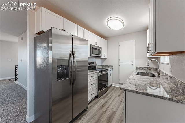 kitchen featuring sink, white cabinetry, dark stone counters, stainless steel appliances, and light hardwood / wood-style floors