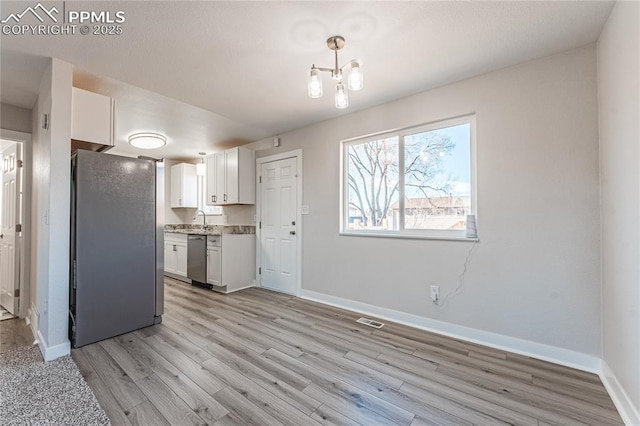 kitchen featuring sink, appliances with stainless steel finishes, white cabinetry, hanging light fixtures, and light hardwood / wood-style floors