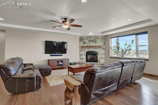 living room with ceiling fan, a tray ceiling, a fireplace, and light hardwood / wood-style flooring