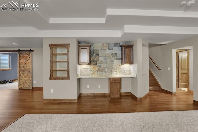 bar with dark hardwood / wood-style floors, a tray ceiling, built in desk, decorative backsplash, and a barn door