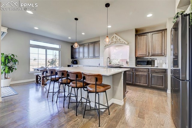 kitchen with decorative light fixtures, tasteful backsplash, stainless steel appliances, a center island with sink, and light wood-type flooring