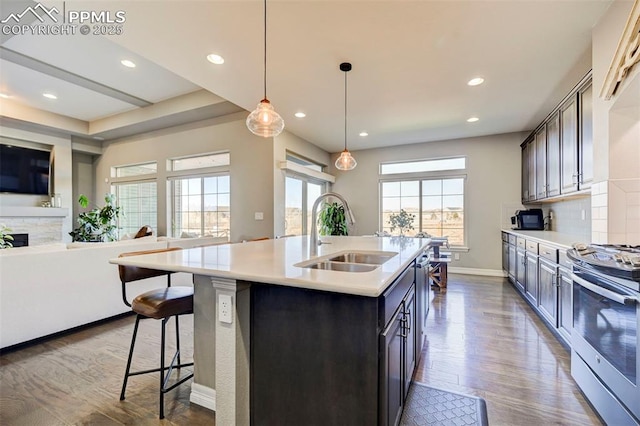 kitchen with sink, hanging light fixtures, dark brown cabinets, a center island with sink, and stainless steel range oven