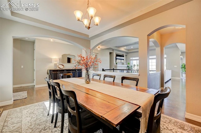 dining space featuring wood-type flooring, a raised ceiling, and a chandelier