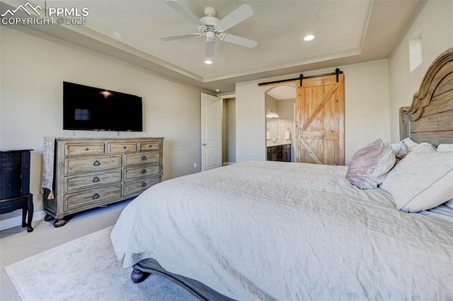 carpeted bedroom with a raised ceiling, ceiling fan, a barn door, and ensuite bath