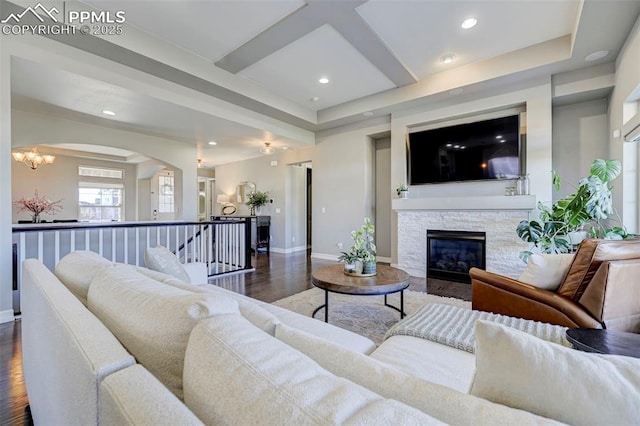 living room with a stone fireplace, beamed ceiling, coffered ceiling, dark wood-type flooring, and an inviting chandelier