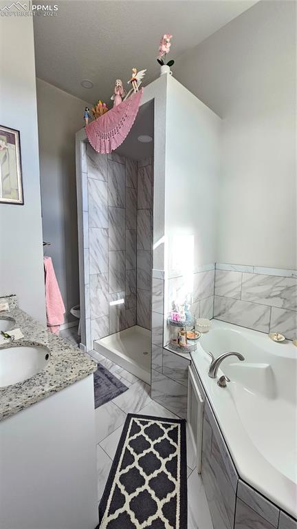 bathroom with a garden tub, marble finish floor, a tile shower, and vanity