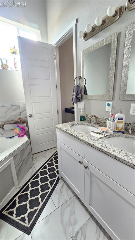 full bathroom featuring double vanity, marble finish floor, a garden tub, and a sink