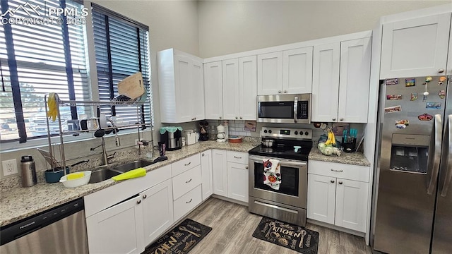 kitchen featuring stainless steel appliances, backsplash, white cabinets, and light wood-style flooring