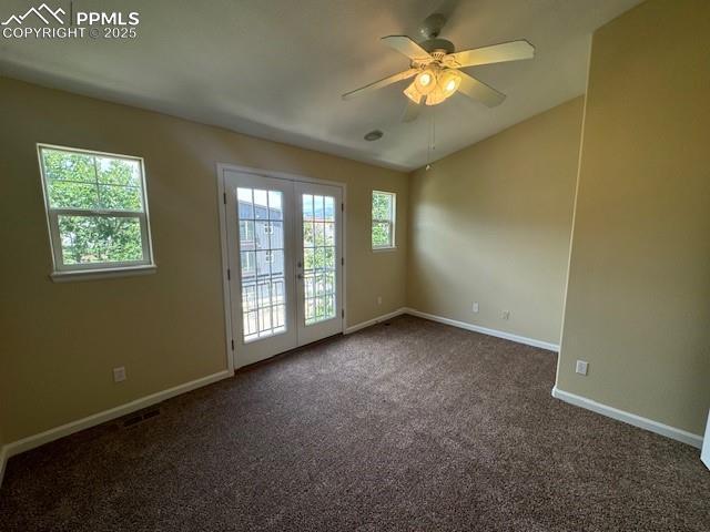 spare room featuring french doors, ceiling fan, a healthy amount of sunlight, and dark colored carpet