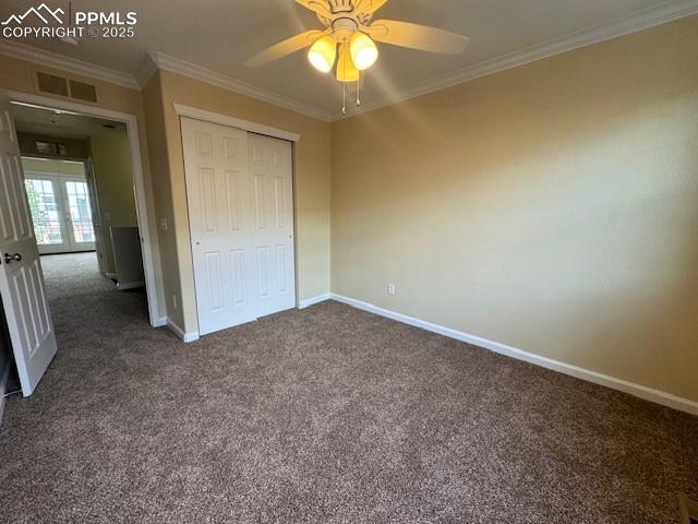 unfurnished bedroom with dark colored carpet, ornamental molding, ceiling fan, and a closet