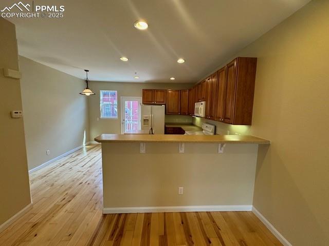 kitchen with a kitchen bar, kitchen peninsula, pendant lighting, white appliances, and light hardwood / wood-style floors