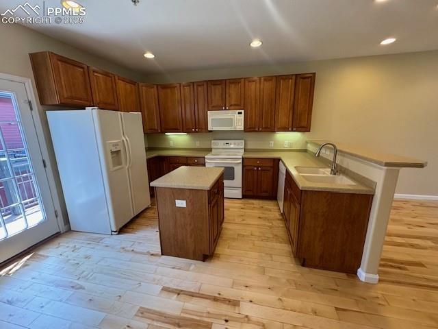 kitchen with light hardwood / wood-style flooring, plenty of natural light, kitchen peninsula, a kitchen island, and white appliances