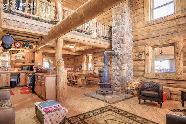 living room featuring a wood stove, light hardwood / wood-style flooring, log walls, and a towering ceiling