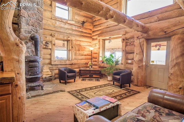 living room featuring a high ceiling, a wood stove, hardwood / wood-style floors, and log walls