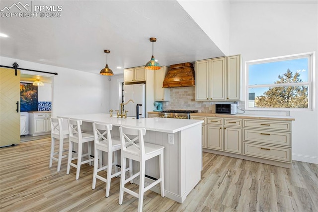 kitchen with custom exhaust hood, an island with sink, pendant lighting, a barn door, and cream cabinetry